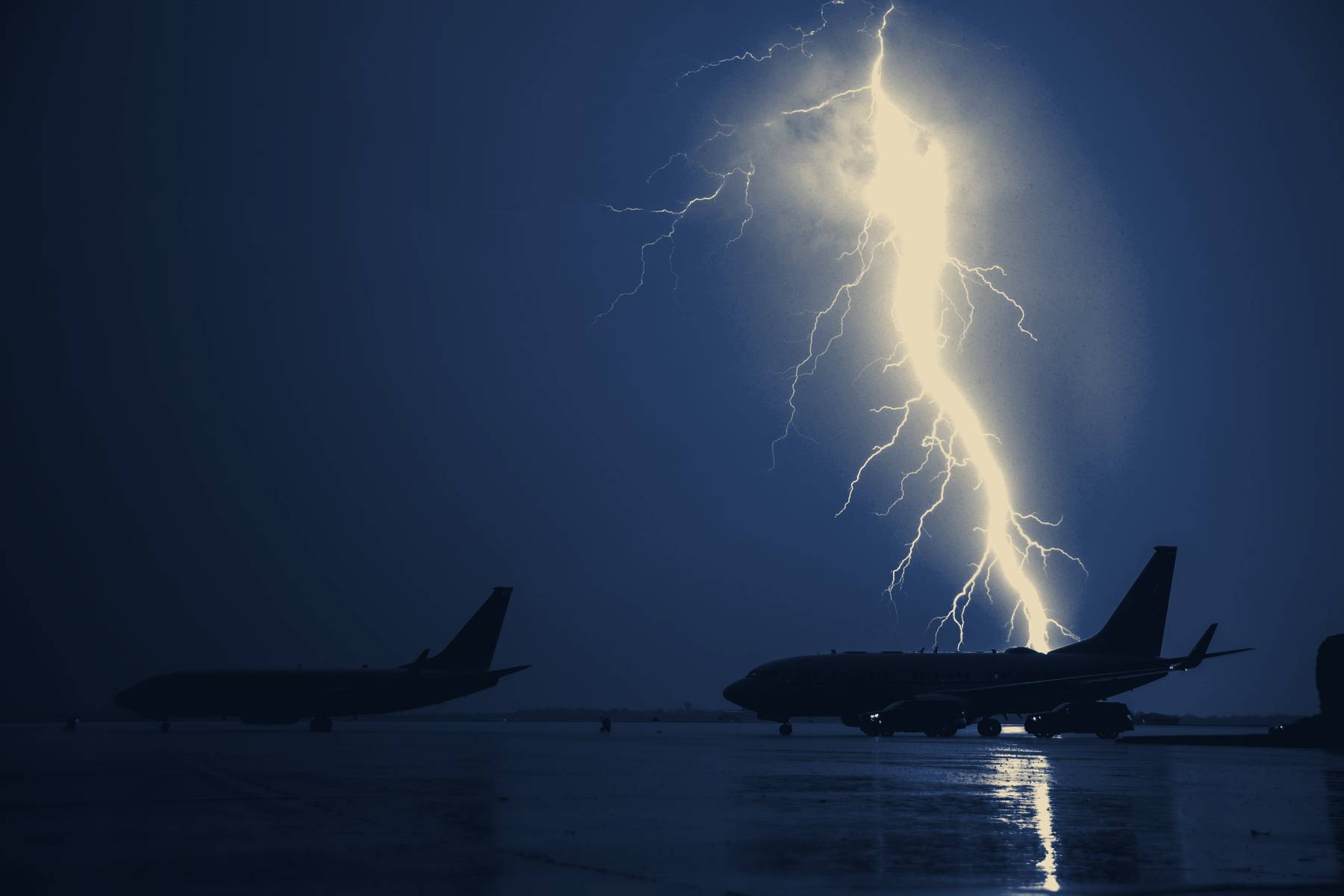 Lightning striking behind two aircraft on a wet flightline