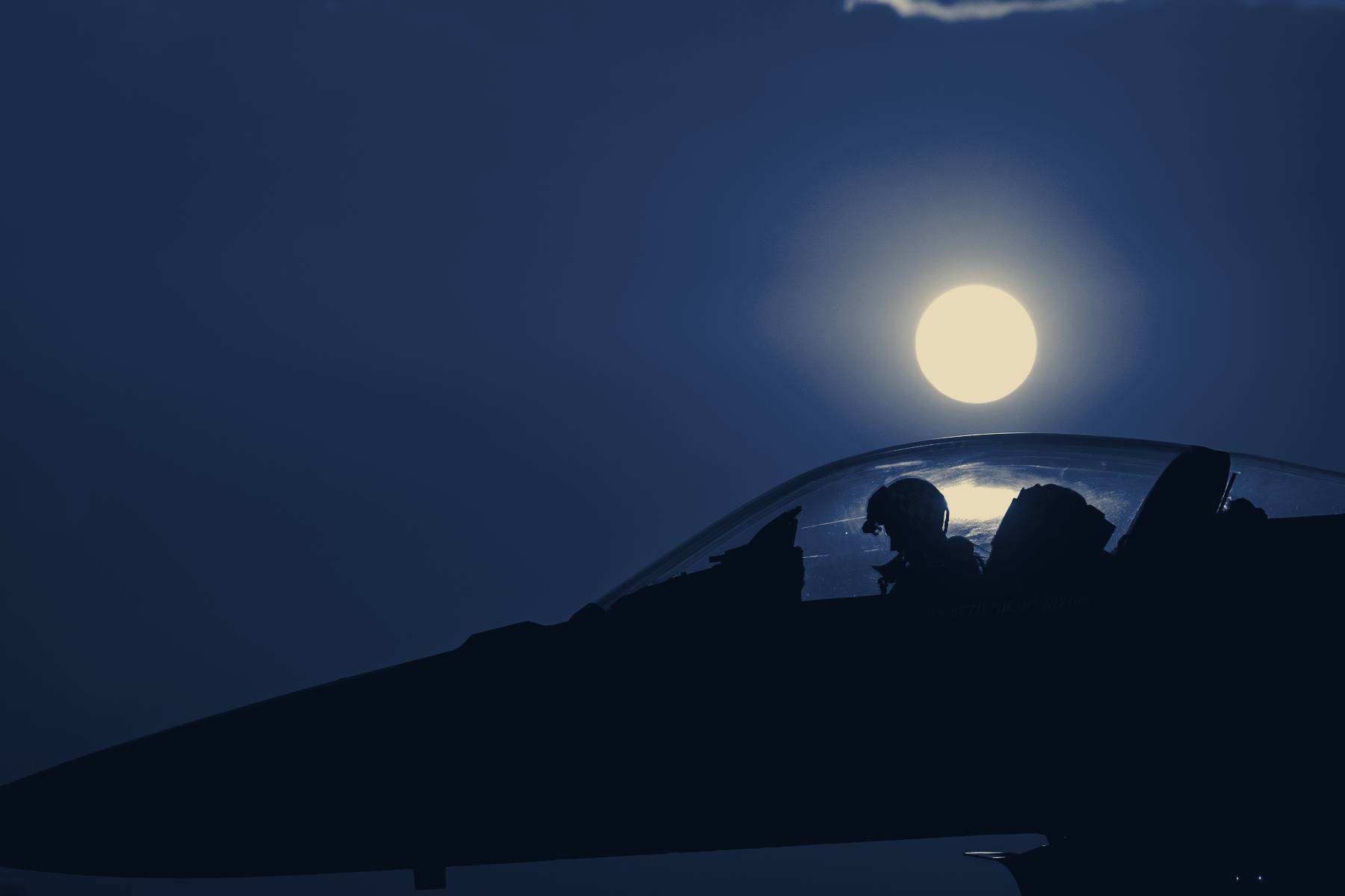 A pilot in an open cockpit against the setting sun
