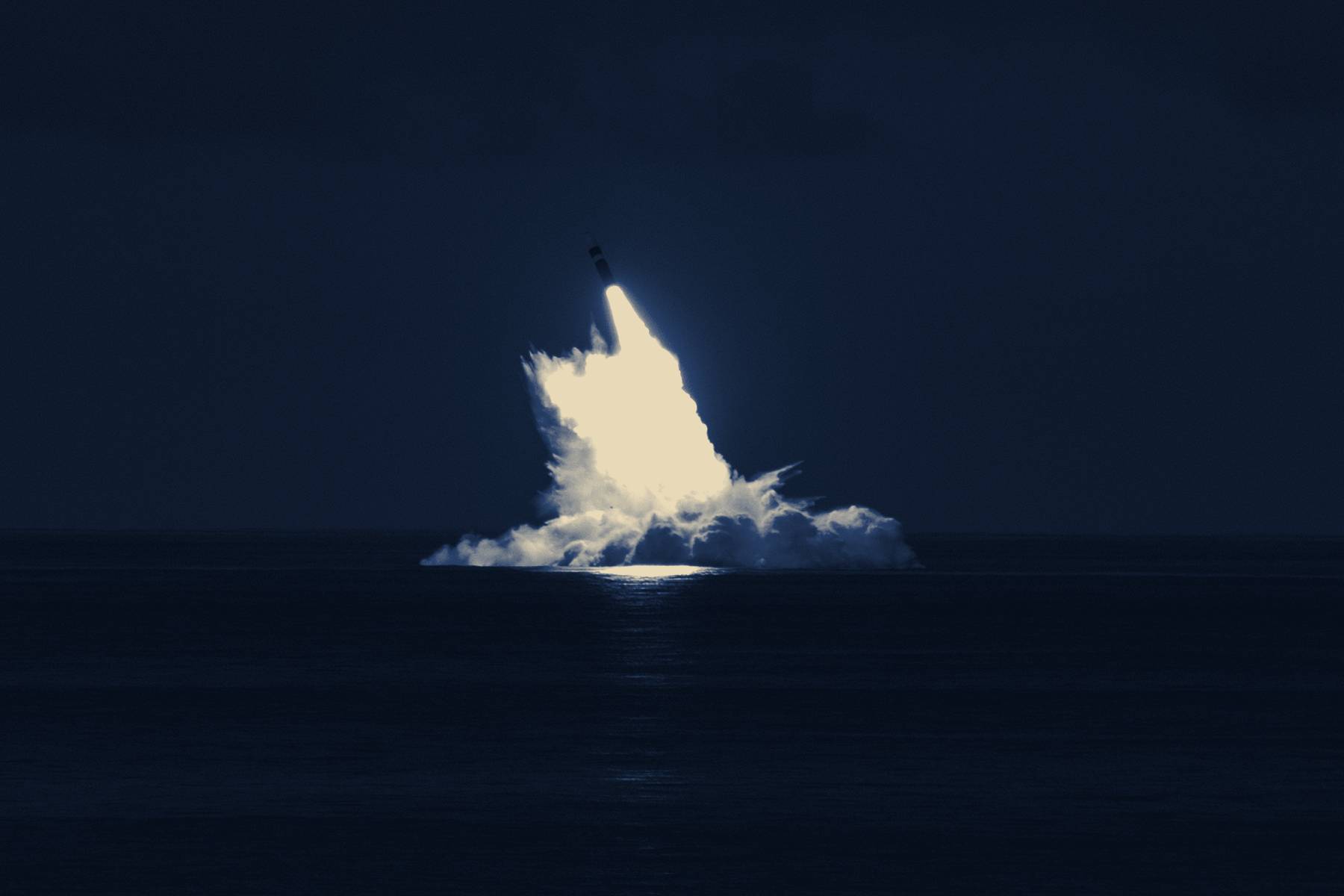 A missile breaking the surface of the sea in a column of fire
